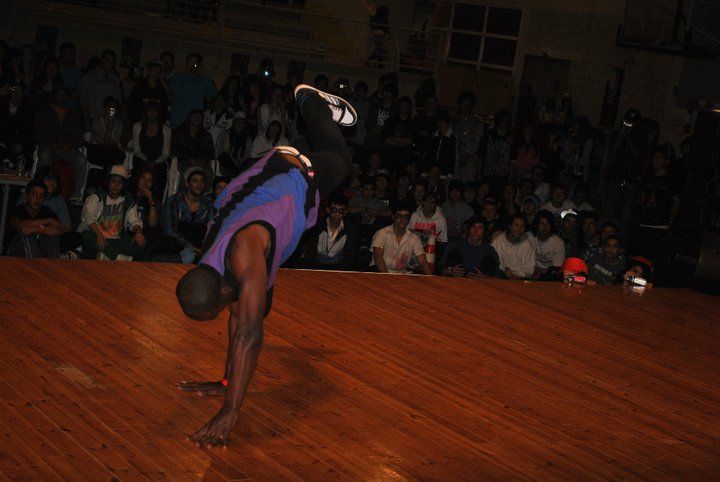 A dancer holding a freeze on a wooden floor in front of a seated crowd