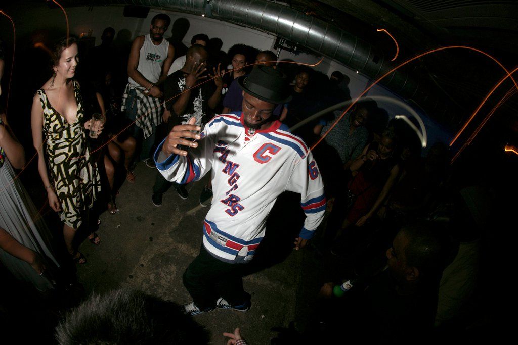A night-time cypher, a dancer in a jersey surrounded by onlookers