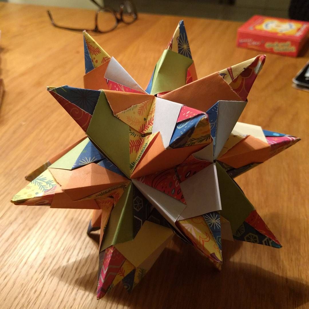 A large spiked modular origami star folded from patterned paper, on a wooden floor