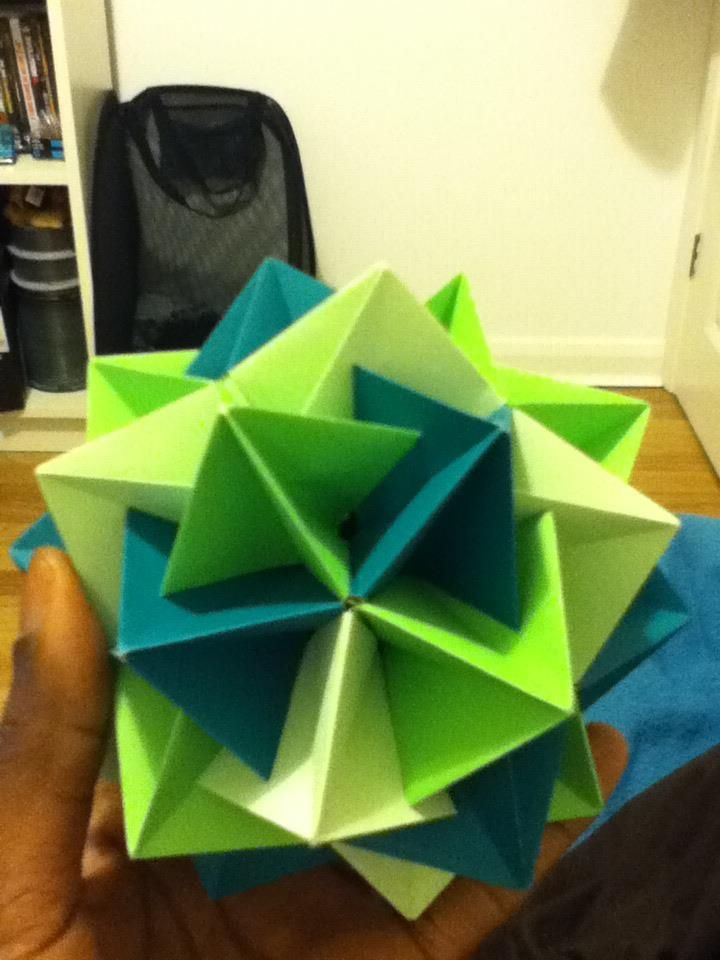 A green and teal spiked modular origami ball held in one hand