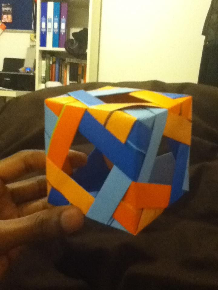 An interlocking blue and orange modular origami cube held in one hand
